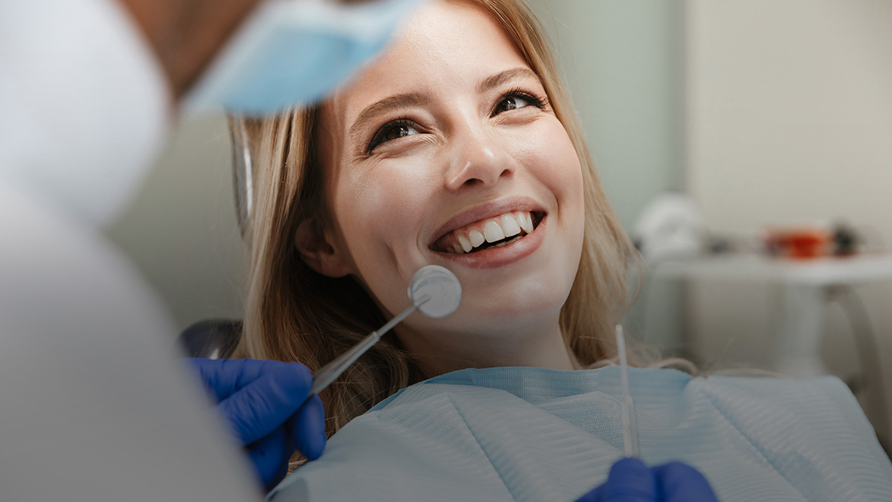 Eine junge Frau sitzt im Behandlungsstuhl eines Zahnarztes. Sie hat ein strahlendes Lächeln.